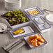 A group of rectangular blue speckled melamine serving bowls with salad and bread on a table.