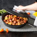A hand using a white towel to lift the cover off a Lodge cast iron skillet full of food.