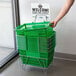 A person holding a green Regency shopping basket with metal handles.