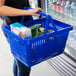 A person holding a Regency Blue plastic shopping basket with food.