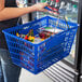 A woman holding a Regency Blue plastic shopping basket full of groceries.