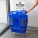 A hand holding a blue Regency plastic grocery shopping basket.