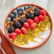 A bowl of yogurt topped with blueberries, blackberries, raspberries, nuts, and passion fruit.