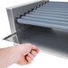 A hand using a Nemco Slanted Hot Dog Roller.