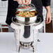 A person using a Vollrath Maximillian steel soup marmite to put pasta into a pot.