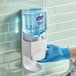 A person in blue gloves using Purell Healthy Soap dispenser.