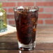 An Anchor Hocking mixing glass filled with brown liquid and ice on a table.