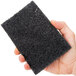 A hand holding a black Scrubble grill polish pad.
