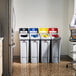 A man sitting at a desk in a room with several Rubbermaid 4-Stream Rectangular Recycling Stations.