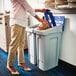 A woman putting a package into a white rectangular recycling bin with a black lid.