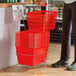A stack of red plastic grocery market shopping baskets with metal handles, placed on a metal stand with a sign.