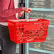 A red plastic grocery market shopping basket with metal handles being carried by a person.