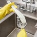 A person in yellow gloves using a Franmara glassware washing brush with foam loop head to clean a glass over a sink.