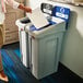 A woman using a Rubbermaid Slim Jim Recycling Lid Insert on a white rectangular trash can.