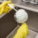 A person in yellow gloves using a Franmara glassware brush to clean a glass over a sink.