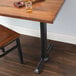 A wooden table with a Lancaster Table & Seating black cast iron end column table base with self-leveling feet and a glass of alcohol on it.