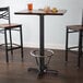 A Lancaster Table & Seating black cast iron bar height table base with a metal foot ring and self-leveling feet.