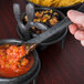 A person using an HS Inc. charcoal polyethylene condiment spoon to scoop salsa from a bowl.