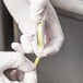 A person in white gloves using a yellow rectangular Hydrion pH test paper dispenser.