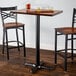 A Lancaster Table & Seating black cast iron bar height table base with beer glasses on a wooden table.