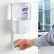 A person using a white Purell automatic hand sanitizer dispenser.