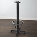 A Lancaster Table & Seating black cast iron bar height table base with a round metal foot ring.