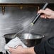 A person using a Matfer Bourgeat stainless steel whisk to mix ingredients in a bowl.