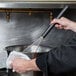 A person using a Matfer Bourgeat stainless steel whisk to stir a pot.