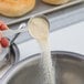 A person using a measuring spoon to scoop white powder from a white bowl.