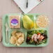 A Carlisle green 6 compartment tray with a sandwich, pear and cup of water.