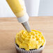 A cupcake with yellow frosting piped using an Ateco basketweave piping tip.