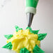 A person using an Ateco leaf pastry tip with green and yellow icing to decorate a cupcake.