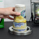 A hand placing a San Jamar stainless steel cup in a cup organizer on a counter.