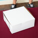 A person holding a 6" x 6" x 2 1/2" white pie / bakery box.