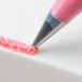 A close-up of a pink pastry bag with pink frosting and a cross-top pastry tip.