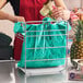 A chrome t-shirt bag rack stand holding a green plastic shopping bag at a checkout counter.