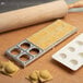 A metal tray with ravioli and a rolling pin on a table.