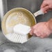 A hand holding a Carlisle Sparta pot scrub brush washing a pan.