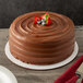 A 12" corrugated white cake circle on a table in a bakery display with a chocolate cake topped with strawberries and blueberries.