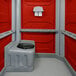 A PolyJohn wheelchair accessible portable restroom with red and grey walls.