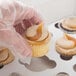 A hand holding a Baker's Mark white mini cupcake box with a cupcake inside.