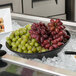 A G.E.T. Enterprises Bugambilia black resin-coated aluminum bowl of grapes on ice.