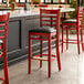 A Lancaster Table & Seating mahogany wood bar stool with a black vinyl seat.