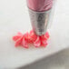 A Ateco pastry bag with pink frosting on a cake decorated with pink flowers.