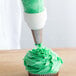 A person using an Ateco drop flower piping tip with green icing to decorate a cupcake.