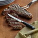 A steak with a Mercer Culinary Genesis® steak knife on a cutting board.