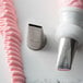 A white and silver Ateco Ribbon Piping Tip next to a pink icing tube with a pink ribbon on a counter.