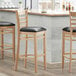 A Lancaster Table & Seating wood ladder back bar stool with a black vinyl seat detached.