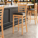 A Lancaster Table & Seating wooden bar stool with a black vinyl seat.