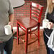 A man and woman holding coffee cups in front of a Lancaster Table & Seating mahogany wood ladder back bar stool with mahogany wood seat.